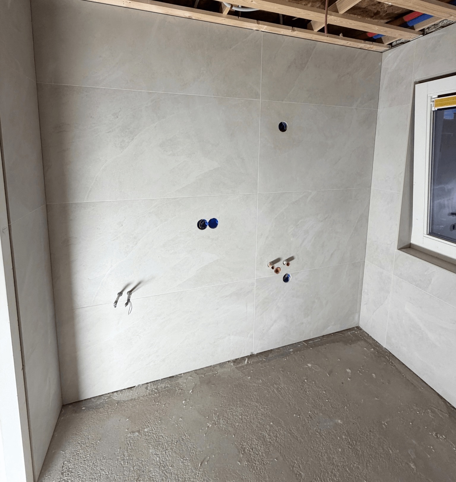 Betegelde wand tijdens de werkzaamheden, nog zonder sanitair en met zichtbare leidingdoorvoeren.